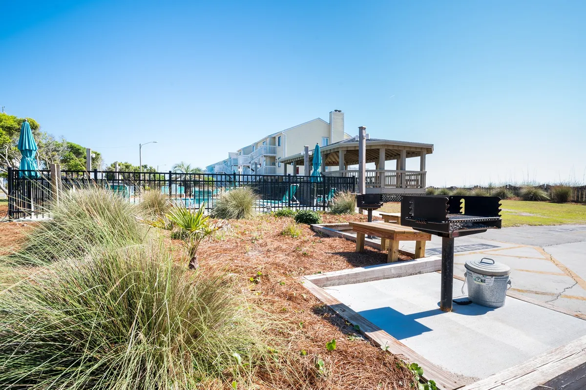 A relaxed outdoor grill and picnic area adjacent to the pool, featuring a barbecue grill, picnic table, landscaped greenery, and the inviting pool in the background.