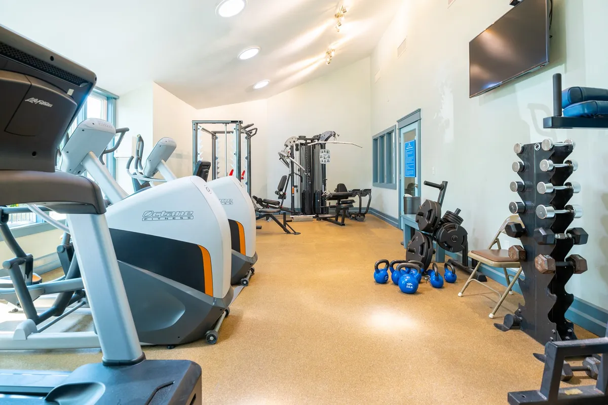 A well-equipped fitness center interior with treadmills, elliptical machines, weights, and mats, all arranged in a bright, motivational setting for a range of exercise routines.