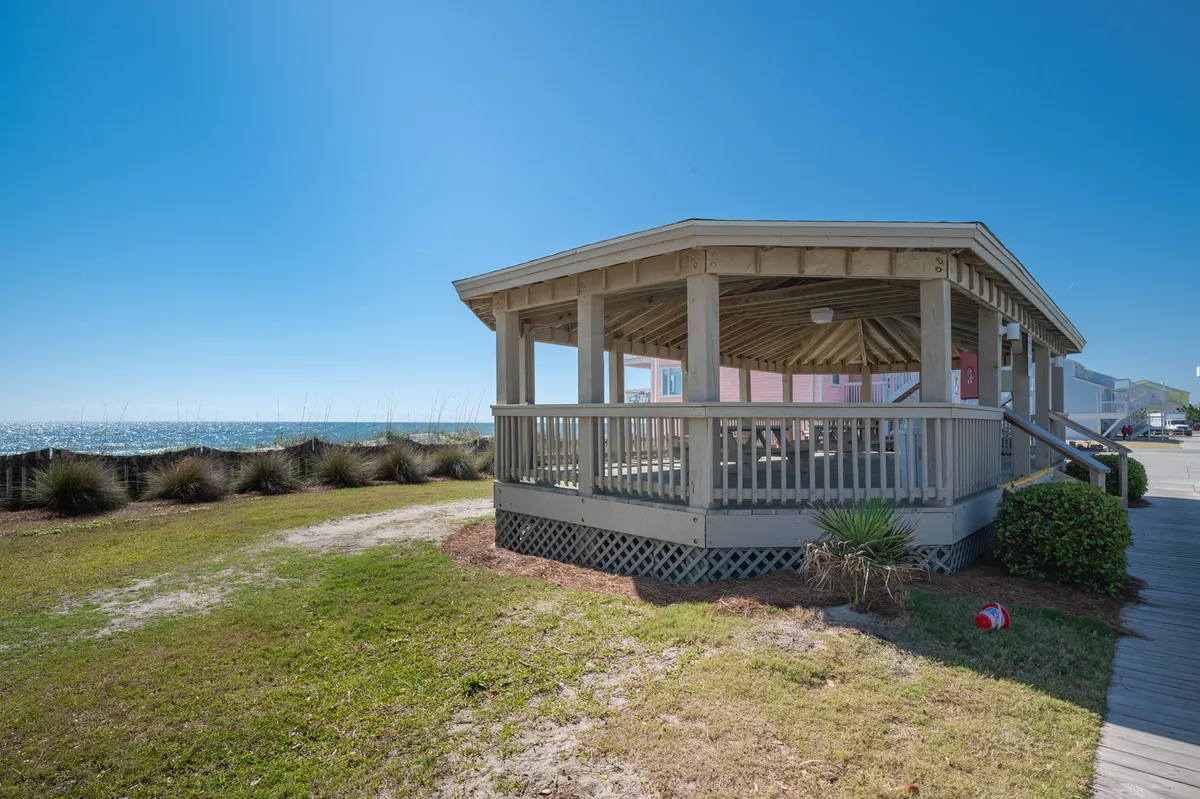 A pavilion structure stands against the backdrop of the ocean, surrounded by lush landscape greenery. The scene suggests a peaceful location for picnics, gatherings, or quiet strolls along the shore, with the ocean in clear view.