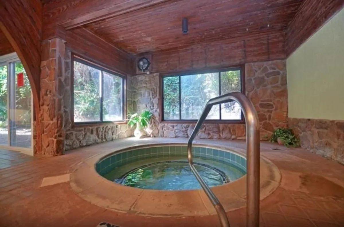 A tranquil indoor hot tub space featuring natural stone walls, lush indoor plants, and large windows that let in soothing light, creating an atmosphere of rejuvenation and calm.