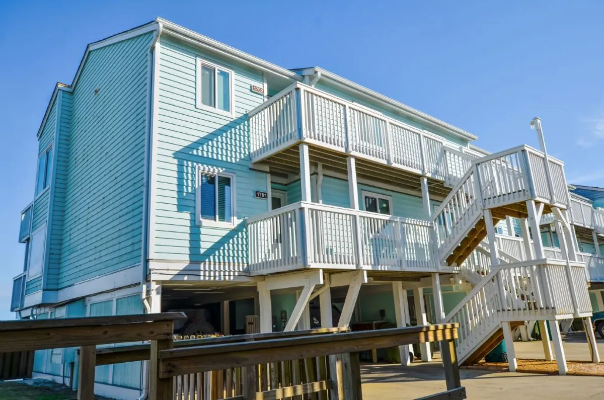 A cheerful exterior shot featuring the building’s light blue facade, white railings, and an exterior staircase leading up to the units. The visible entry points reinforce the idea of private, secure access.